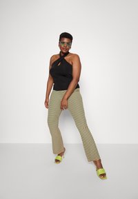 Top halter preto com recorte em forma de olho, calças largas listradas em verde, amarelo e vermelho, combinadas com sandálias de salto alto verde brilhante.