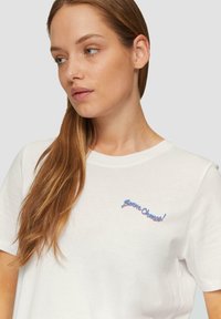 White cotton t-shirt featuring a blue and red embroidered phrase "Bonne Chance!" positioned on the left chest. Short sleeves, crew neck design.