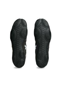 Zapatillas deportivas negras con suelas de goma texturizada que presentan patrones circulares concéntricos y agarres en zigzag, acentuadas con elementos de diseño en blanco.