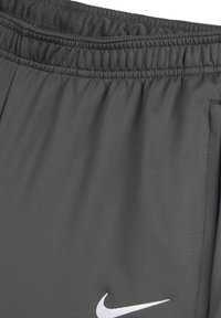 Pantaloni sportivi grigi con una vita elasticizzata, realizzati in tessuto liscio, con un logo Nike bianco sulla parte inferiore sinistra.