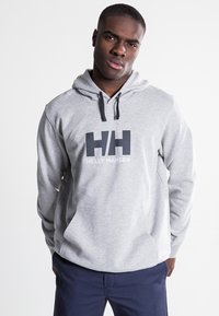 Sudadera gris con capucha y un bolsillo canguro en el frente, con un gran logo "HH" en azul oscuro y el texto blanco "HELLY HANSEN". Detalles con cordón.