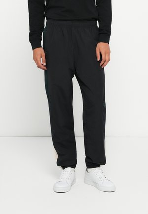 Pantaloni de jogging negri, ușori, cu talie elastică. Prezintă o croială conică și manșete ribbate. Asortați cu adidași albi pentru un contrast.
