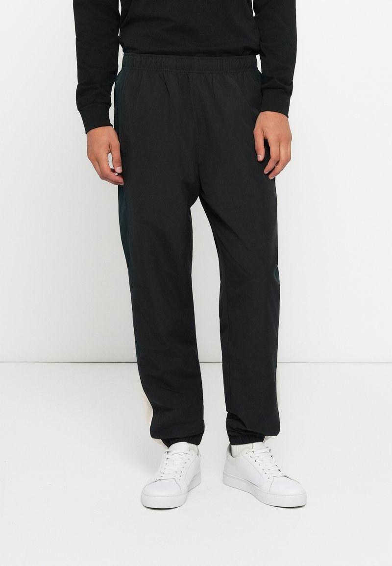 Black, lightweight joggers with an elastic waistband. Features a tapered fit and ribbed cuffs. Paired with white sneakers for contrast.