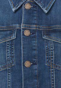 Jeansjacka i mörkblått, med standardkrage, bronsknappar, kontrasterande orange sömmar och en fickdetalj på vänster sida.