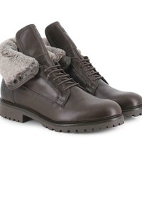 Botas de cuero marrón con un cuello doblado de piel sintética, punta redonda y suela de goma texturizada. Cuentan con cordones y ojales metálicos.