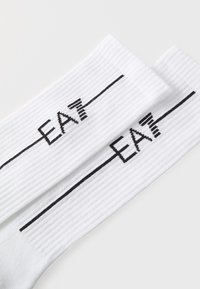 Calzini bianchi a coste con testo nero "EAT" e design a linee orizzontali. Tessuto morbido con una texture che migliora il comfort e la vestibilità.