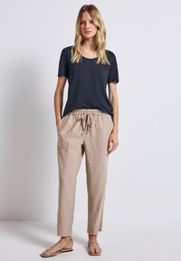 Námořnické tričko s krátkým rukávem v kombinaci s volnými béžovými lněnými kalhotami se strečovým pasem a dvěma předními kapsami. Na nohou má ploché sandály.