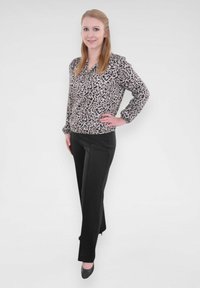 Blouse à imprimé léopard avec des manches longues, en tissu léger ; pantalons noirs ajustés à jambe droite et léger éclat. Talons noirs.