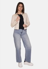 Giacca di pelle beige con un design aderente, abbinata a un top nero e jeans a gamba larga blu chiaro. Sneakers bianche completano il look.