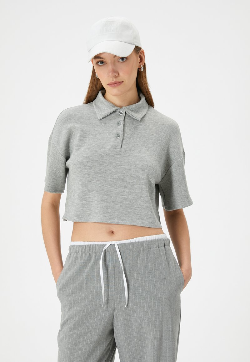 Lys grå, cropped polo shirt med korte ærmer og krave, udstyret med tre knaplukninger og blød tekstur, parret med matchende stribede bukser.