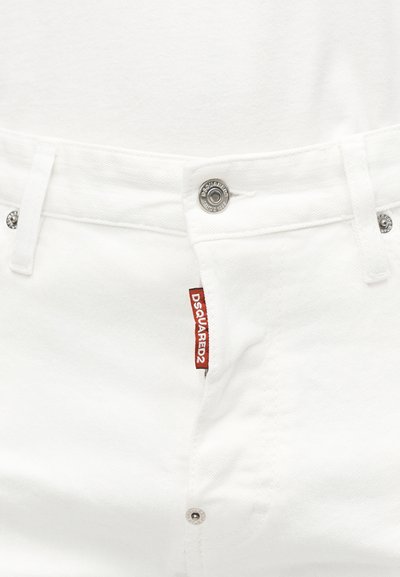 Gros plan sur un jean en denim blanc montrant un bouton et des rivets argentés, des passants de ceinture et une étiquette en tissu rouge avec le logo "DSQUARED2".