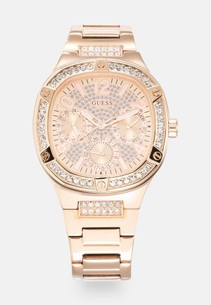 Montre Guess avec un bracelet en acier inoxydable rose doré, un cadran texturé avec des embellissements en cristal, et trois sous-cadrans pour la date et l'heure.