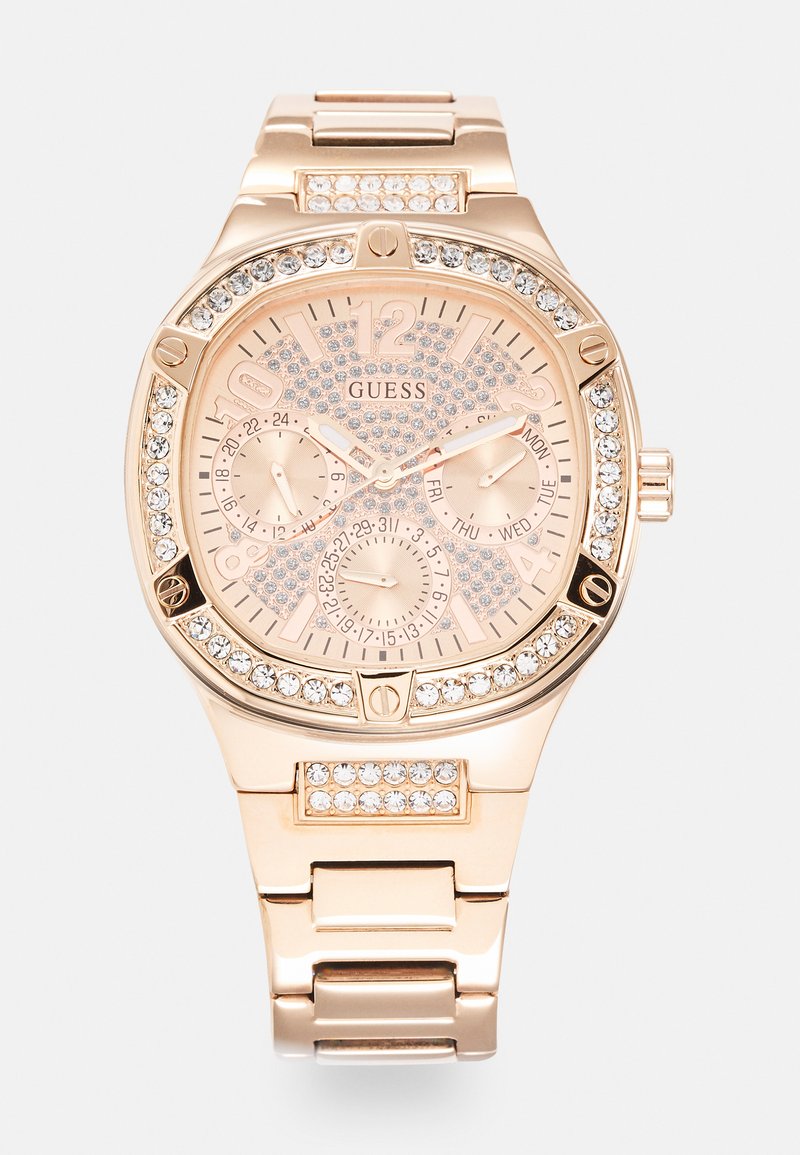 Montre Guess avec un bracelet en acier inoxydable rose doré, un cadran texturé avec des embellissements en cristal, et trois sous-cadrans pour la date et l'heure.
