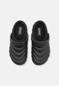 Crocs neri con un esterno in gomma testurizzata, caratterizzati da un design ondulato, fodera morbida nera e una fibbia per una vestibilità sicura.