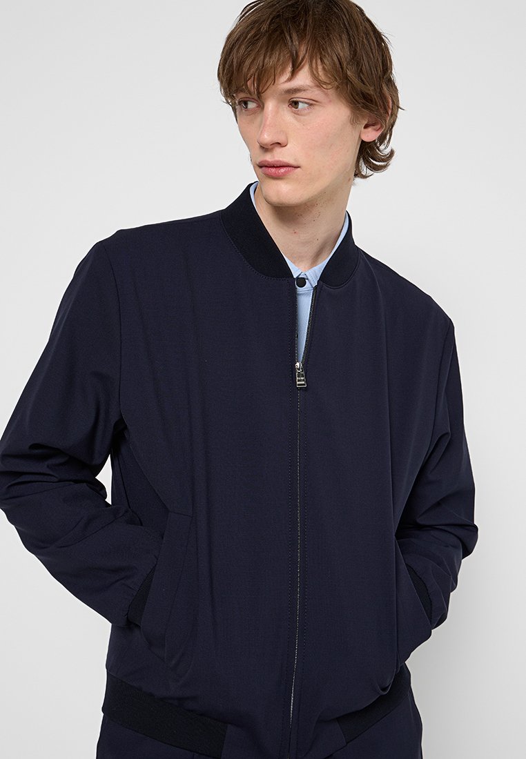 Marineblauer Bomberjacke mit Reißverschluss vorne, geripptem Kragen und Bündchen, zwei Seitentaschen und einer glatten Stoffoberfläche.