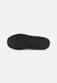 Semelle de sneaker en caoutchouc noir présentant un motif de bande de roulement texturé avec des carrés et des rectangles surélevés pour l'adhérence. Nom de la marque gravé visible.