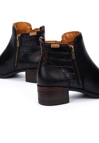Botas de tobillo de cuero negro con un patrón de cocodrilo texturizado, cremalleras doradas, acentos marrones y un tacón de madera apilada.