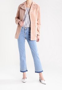Veste en daim rose blush avec col cranté portée sur un haut à rayures, associée à un jean court bleu clair et des mules blanches à talons.