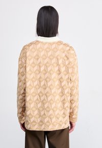 Long-sleeve shirt in beige with a geometric pattern. Features a white collar, ribbed cuffs, and a slightly loose fit. Made from soft fabric.