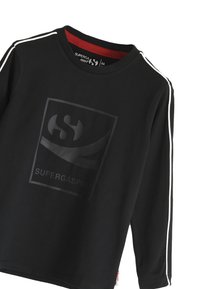 Zwart langlopend t-shirt gemaakt van zacht materiaal, met een glanzend logo in het midden en contrasterende witte strepen op de schouders.