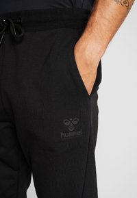 Svarta sweatpants i mjukt tyg med elastisk linning och justerbar dragsko. Inkluderar en sidoficka och präglad logodetalj.