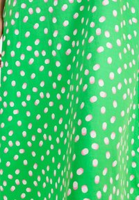 Zielony materiał w białe i różowe owalne grochy. Wzór charakteryzuje się gładką teksturą, tworząc zabawny motyw na całej powierzchni.