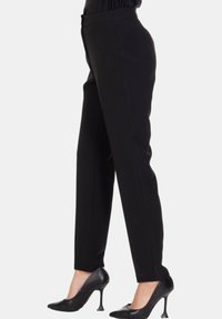 Pantaloni neri sartoriali a taglio aderente, con una texture liscia e vita a mezza altezza, abbinati a scarpe nere con tacco alto.