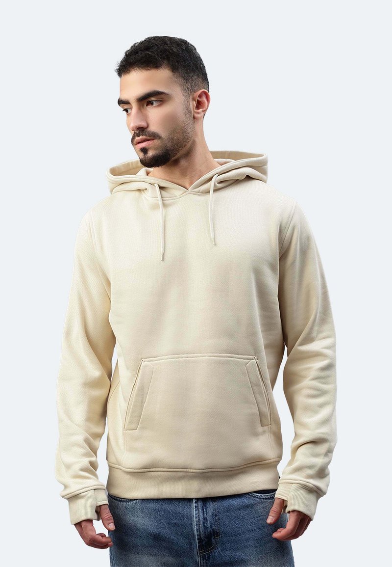 Hoodie beige realizzato in morbido tessuto, con tasca frontale, cappuccio con cordino e polsini a coste, indossato con jeans di denim.