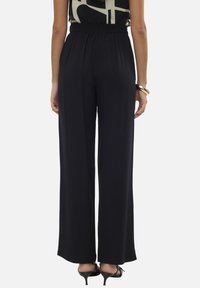 Pantalones de pierna ancha negros, hechos de un tejido ligero, con una cinturilla elástica y una textura suave. Llevados con una blusa de estampado.