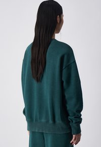 Turkusowa, oversize bluza z miękkiej tkaniny, z opadającymi ramionami i ściągaczami. Posiada klasyczny dekolt okrągły oraz luźny krój.