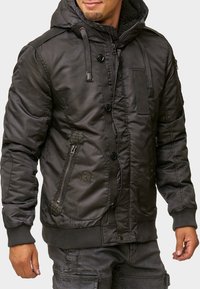 Mörk, vadderad jacka med dragkedja och knappstängning, huva med dragsko och sidofickor. Har kviltade detaljer och ribbade ärmslut.