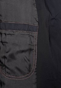 Zwarte stof met een zachte textuur heeft een grote zak, omlijnd met contrasterende roze stiksels aan de linkerkant.