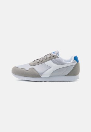 Scarpe sportive con una tomaia in suede grigio e mesh, dettagli bianchi e un tab in blu sul tallone. Presentano una suola testurizzata per una migliore aderenza.