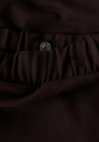 Dark brown fabric with elastic waistband and a black adjustable strap secured by a small black four-hole button.