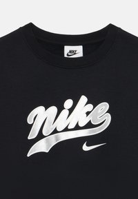 Svart bomull T-skjorte med et stort metallisk sølvfarget "Nike"-logo og en mindre sølvfarget Swoosh, med klassisk rund hals.