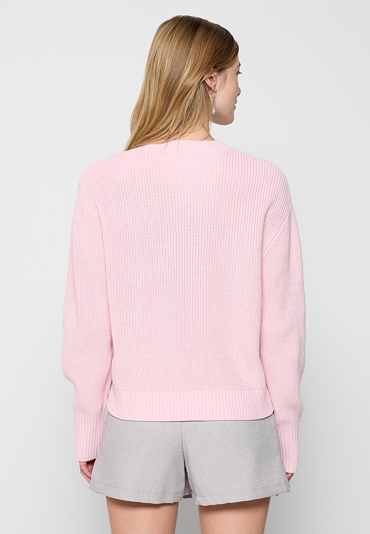 Pull en tricot rose clair avec un col et des poignets côtelés, présentant un motif texturé et une coupe courte au niveau de la taille.