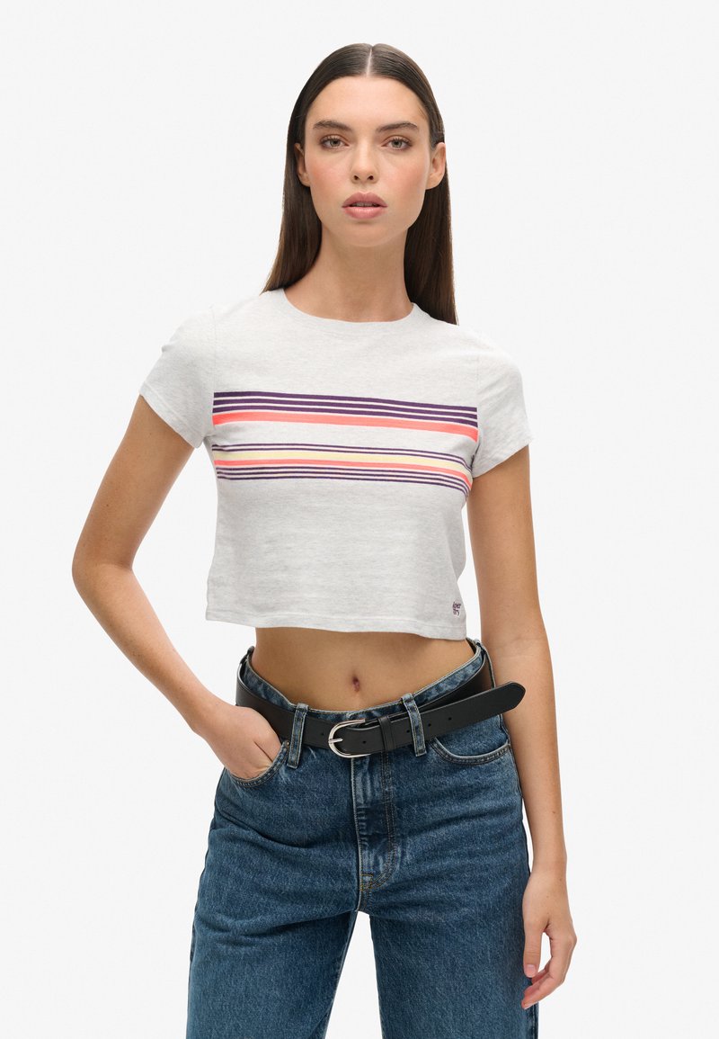Grijs cropped t-shirt met horizontale strepen in roze, paars en koraal. Het model draagt het met een hoge taille blauwe jeans en een zwarte riem.