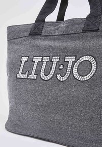 Sac fourre-tout en tissu gris avec des poignées noires et "LIU·JO" écrit en lettres mosaïques réfléchissantes sur le devant.