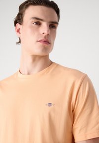 Lys orange bomulds T-shirt med rund hals, afslappet pasform og lille broderet logo på brystet. Glat tekstur, korte ærmer.