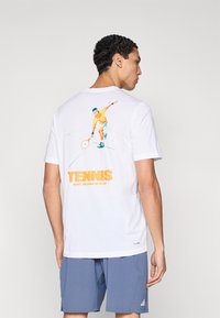 Camiseta blanca de algodón con un gráfico colorido de tenis en la parte trasera. La camiseta tiene mangas cortas y un escote redondo.