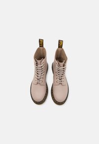 Botas de tobillo de cuero rosa claro con suelas de goma negras, costuras amarillas y tiradores amarillos. Cuenta con un diseño de cordones con ojales.
