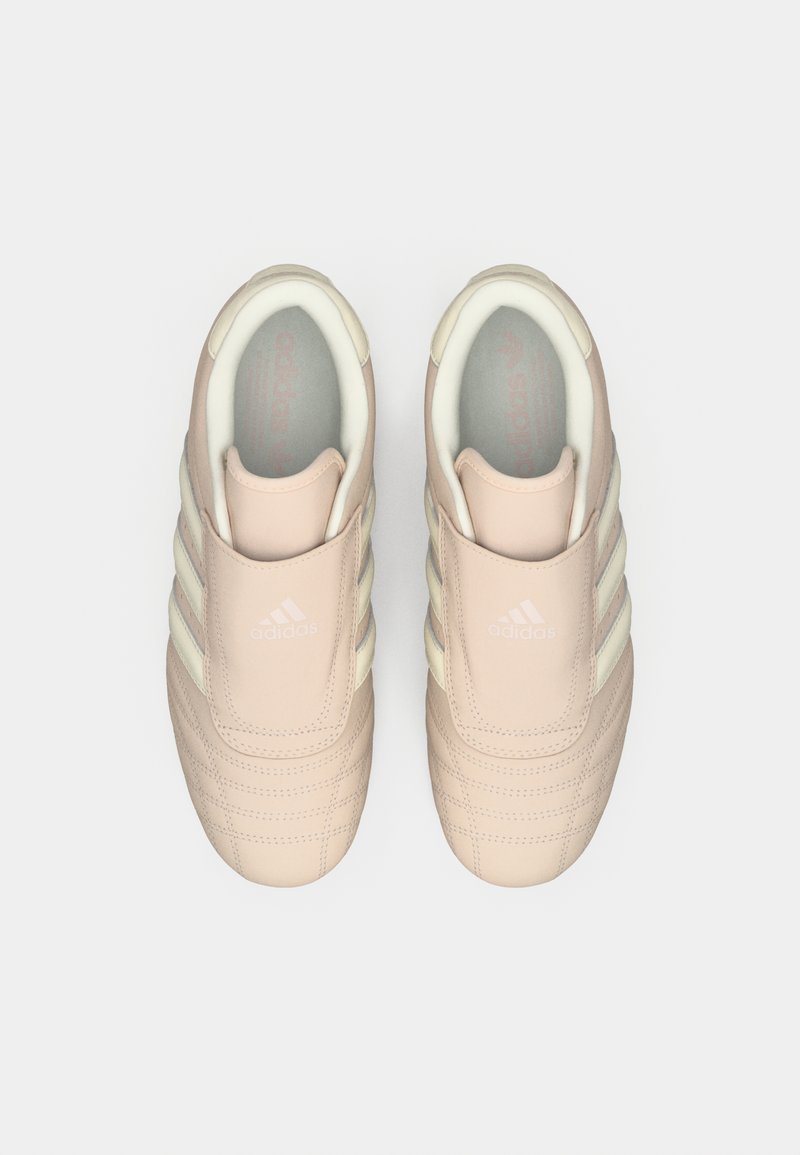 Zapatillas tipo slip-on de color rosa claro con tres rayas blancas, parte superior texturizada, cuello acolchado y logo en relieve en la lengüeta.