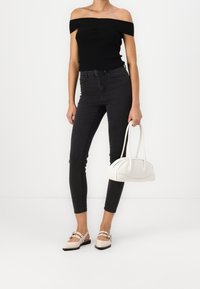 Top negro sin hombros, jeans oscuros ajustados, bolso crema con diseño curvado y bailarinas rosa claro con doble tirante y herrajes decorativos.