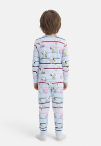 Παιδί που στέκεται με την πλάτη γυρισμένη, φορώντας ανοιζουρογαλανές πιτζάμες με σχέδια από καρτούν Snoopy και Woodstock και πολύχρωμες οριζόντιες ρίγες.