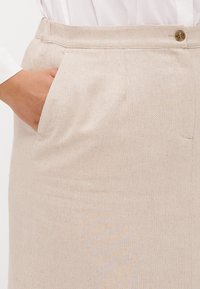 Beige vevd skjørt med en glatt tekstur, sidelommer og en knappelukking i livet, som fremhever det skreddersydde designet.