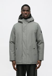 Šedá nepremokavá bunda s kapucňou, so zapínaním na prednej strane pomocou patentiek, dvoma postrannými vreckami a textúrovaným povrchom.