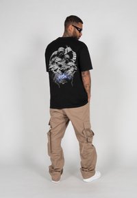 Black t-shirt with graphic design on the back, featuring floral elements and figures. Paired with beige cargo pants and white sneakers.