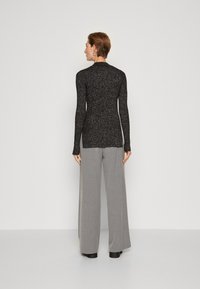 Svart långärmad topp med en texturerad stickad yta, tillsammans med vida grå byxor. Outfitten har en slank, figurnära silhuett.