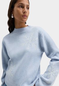 Jasnoniebieski sweter z dzianiny z białymi haftowanymi wzorami płatków śniegu na przodzie i rękawach, z prążkowanym okrągłym dekoltem i luźnym krojem.