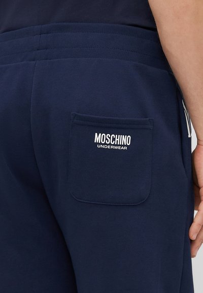 Námornícke modré tepláky s rebrovaným pásom, s zadnou vreckom embosovaným nápisom "MOSCHINO UNDERWEAR" v bielej farbe. Mäkká textúra.